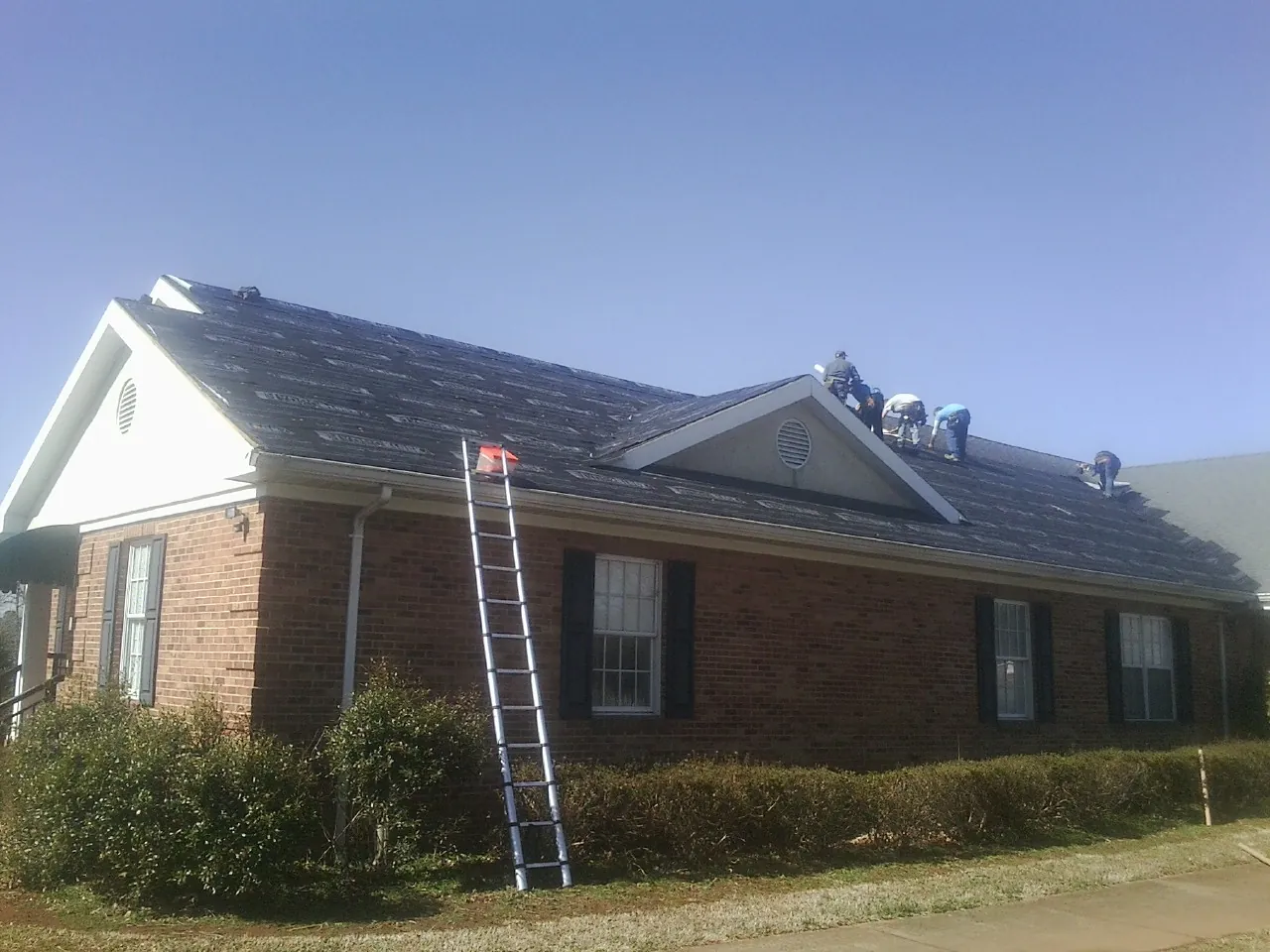 Crew tearing shingles off a brick ranch roof with a ladder set — Emergency Roof Repair work by our crew in Cokato