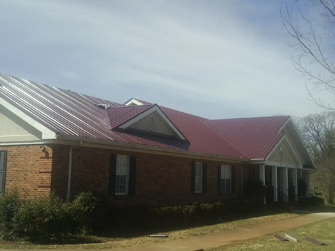 Red metal roof with gabled entries on a long brick building, from a Hail Damage Roof Repair job in Cokato