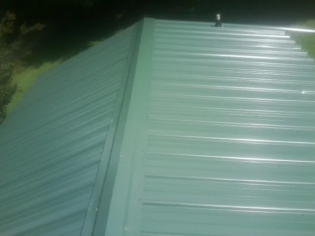 New green metal panels meeting at the ridge of a roof — Flat Roof Repair work by our crew in Cokato