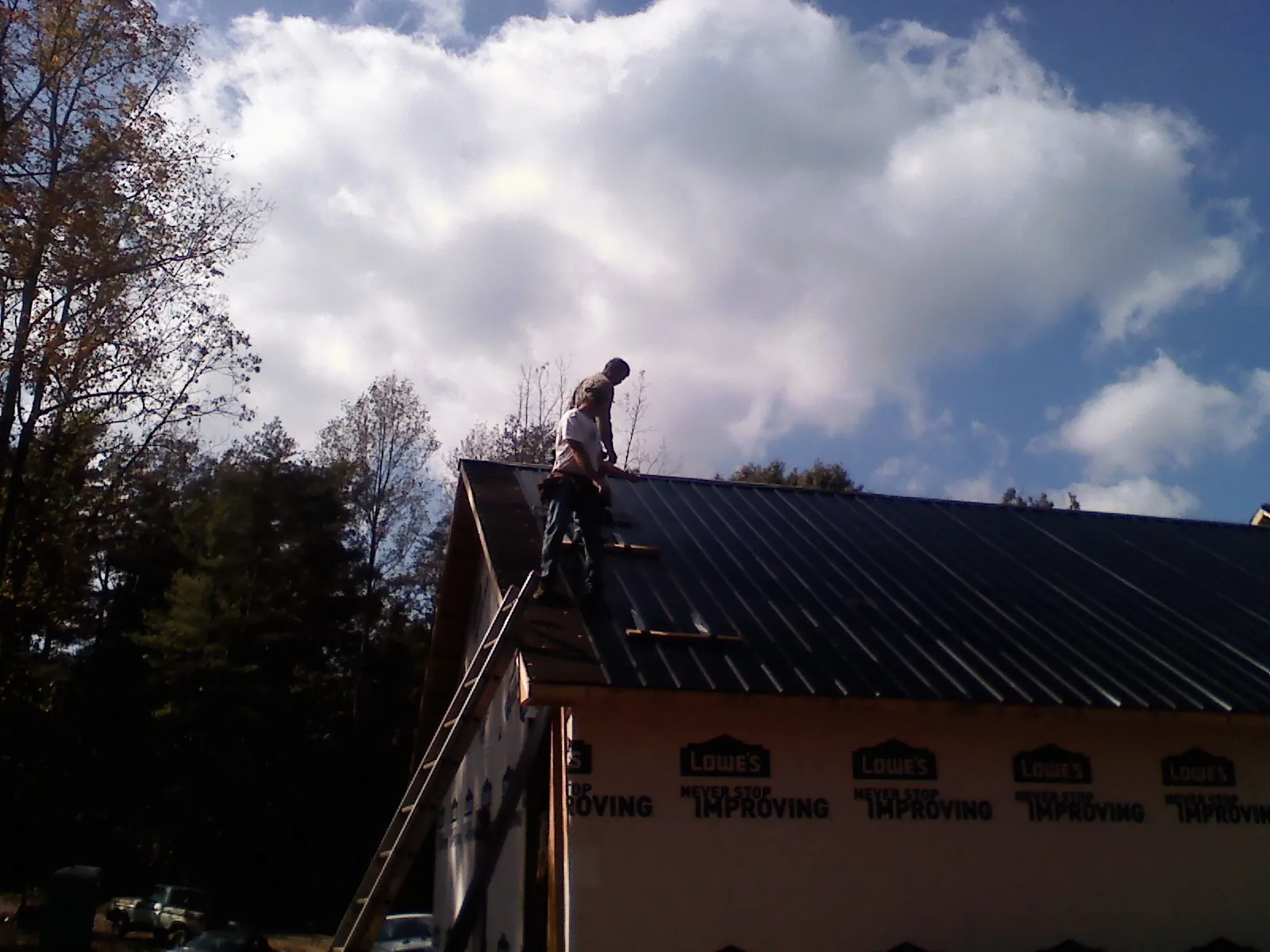 Roofer fastening dark metal panels high against a cloudy sky, from a Roof Inspection job in Cokato