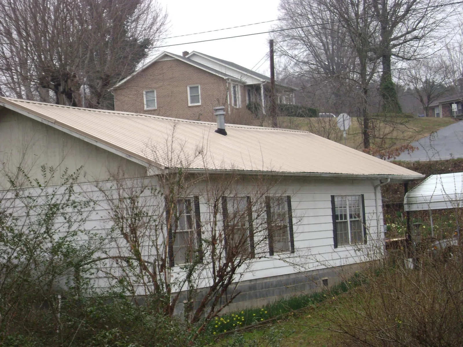 Tan metal roof on a white sided house set into a hillside — Commercial Roofing by Roofing Brothers in Cokato