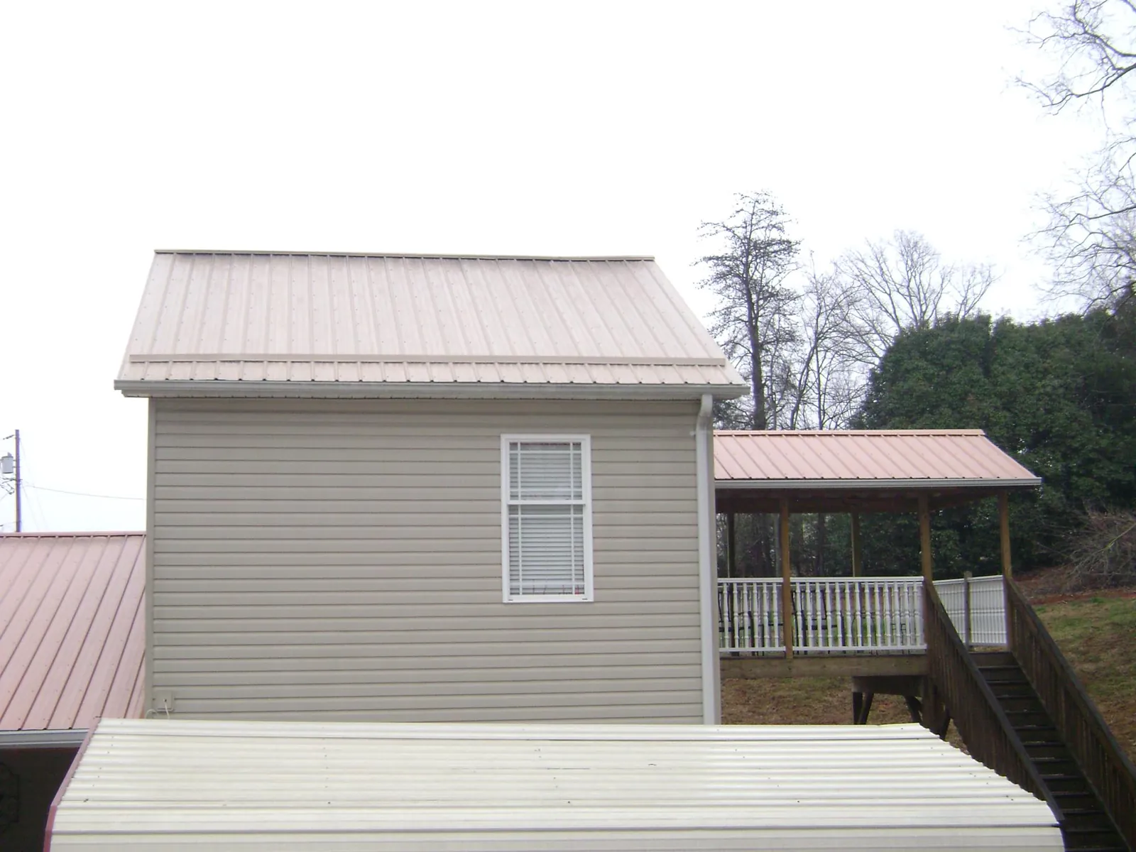 Tan metal roofs on a two story addition and attached porch, from a Roof Replacement job in Cokato